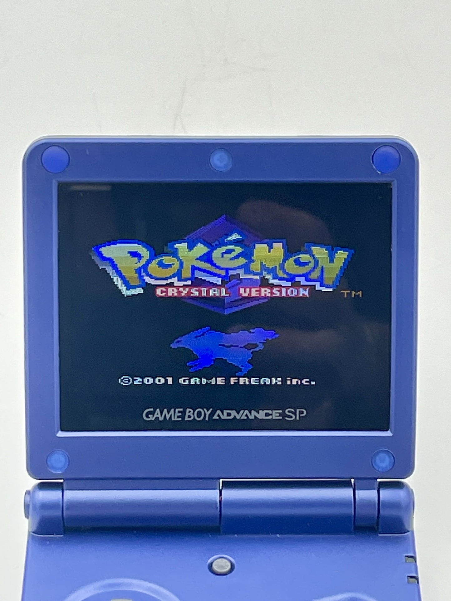 Blue Game Boy Advance SP displaying the 'Pokémon Crystal Version' title screen on a white background.