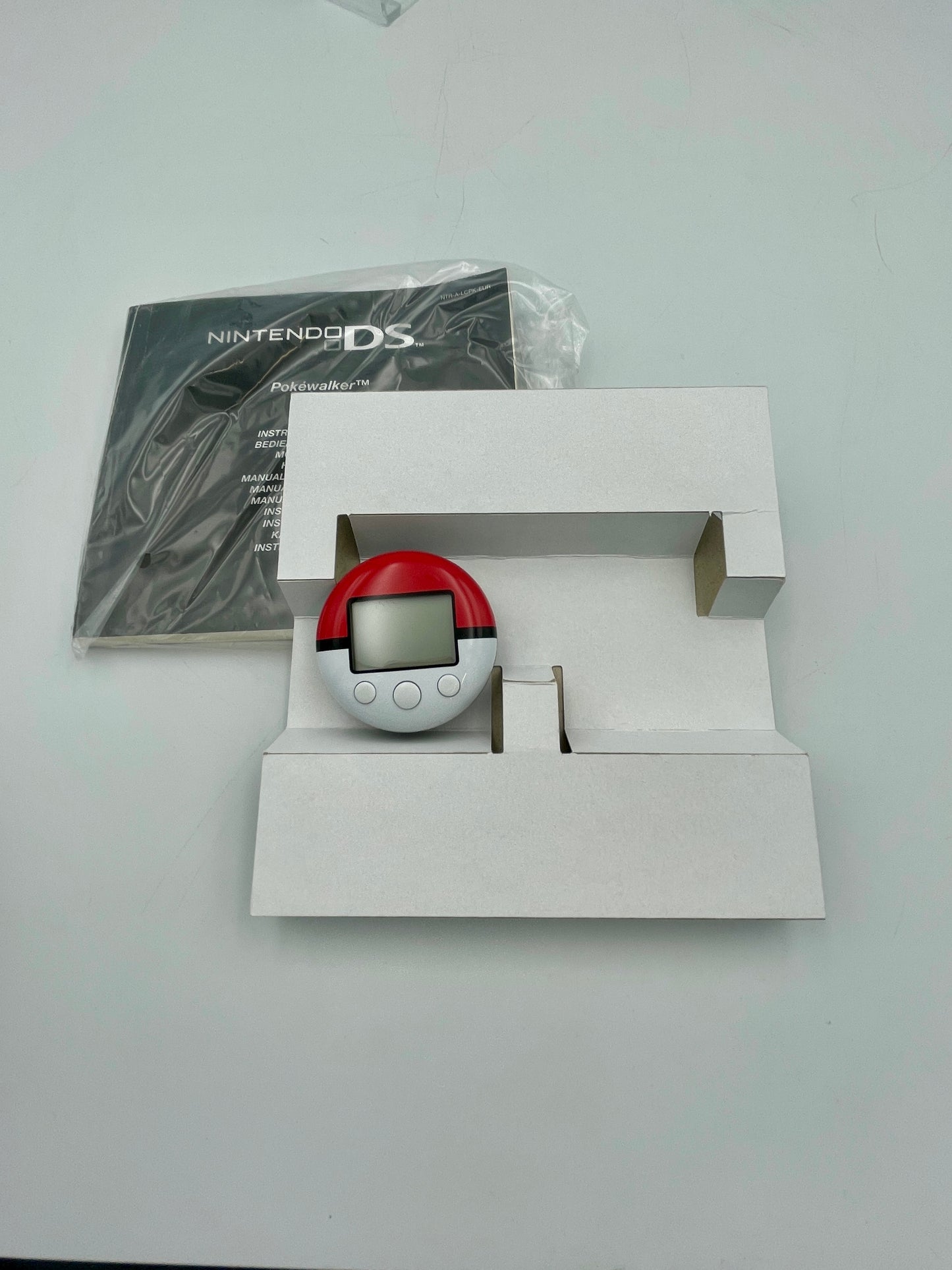 Pokéball in a white box with a Nintendo DS manual on a light gray background