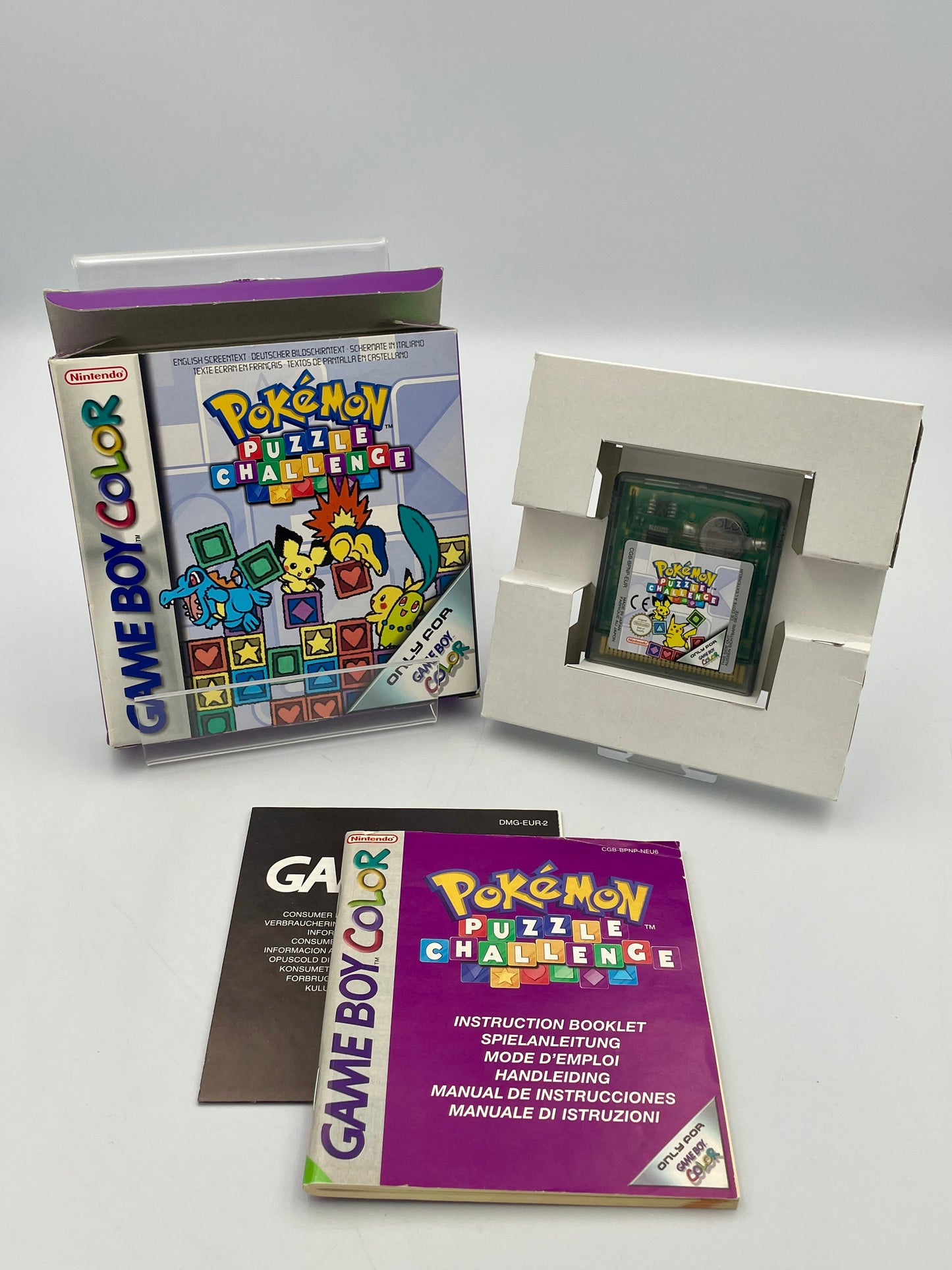 Nintendo Game Boy Color with 'Pokémon Puzzle Challenge' cartridge and manual on a gray background