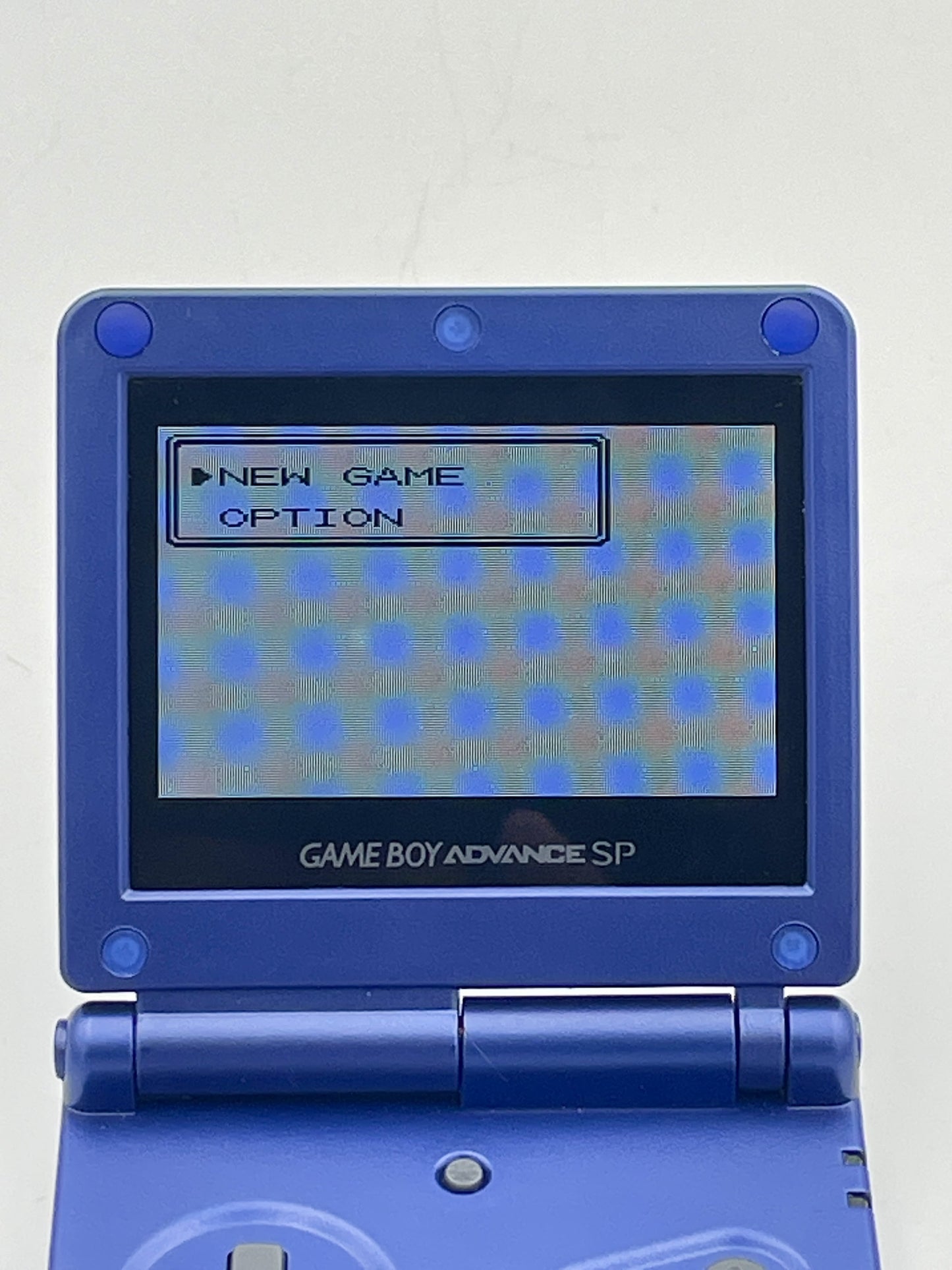 Blue Game Boy Advance SP with screen displaying game menu on a light gray background