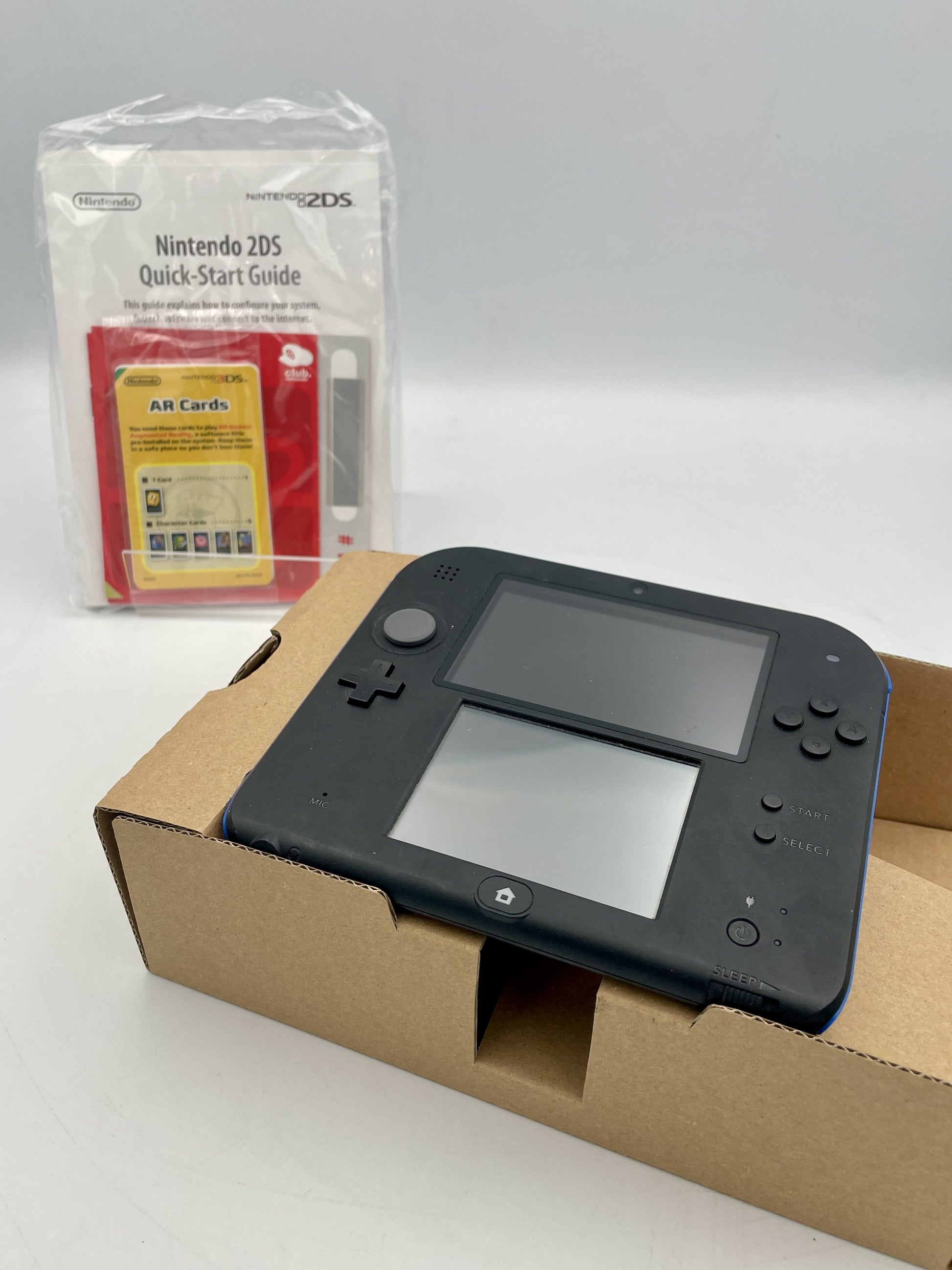 Black Nintendo 2DS gaming console with a quick-start guide on a white background