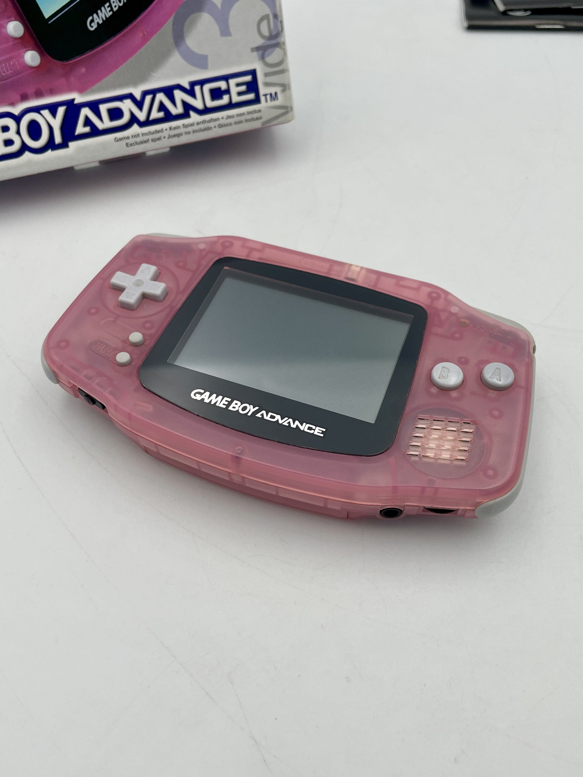 Pink Game Boy Advance console on a white surface with packaging in the background.
