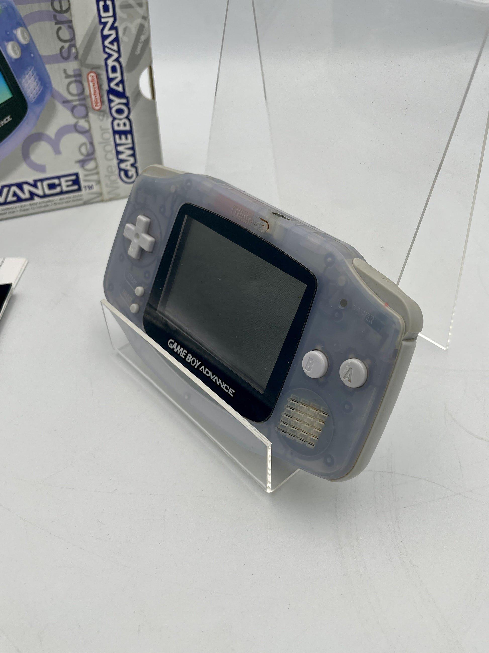 Gray Game Boy Advance console on a white surface with packaging in the background.