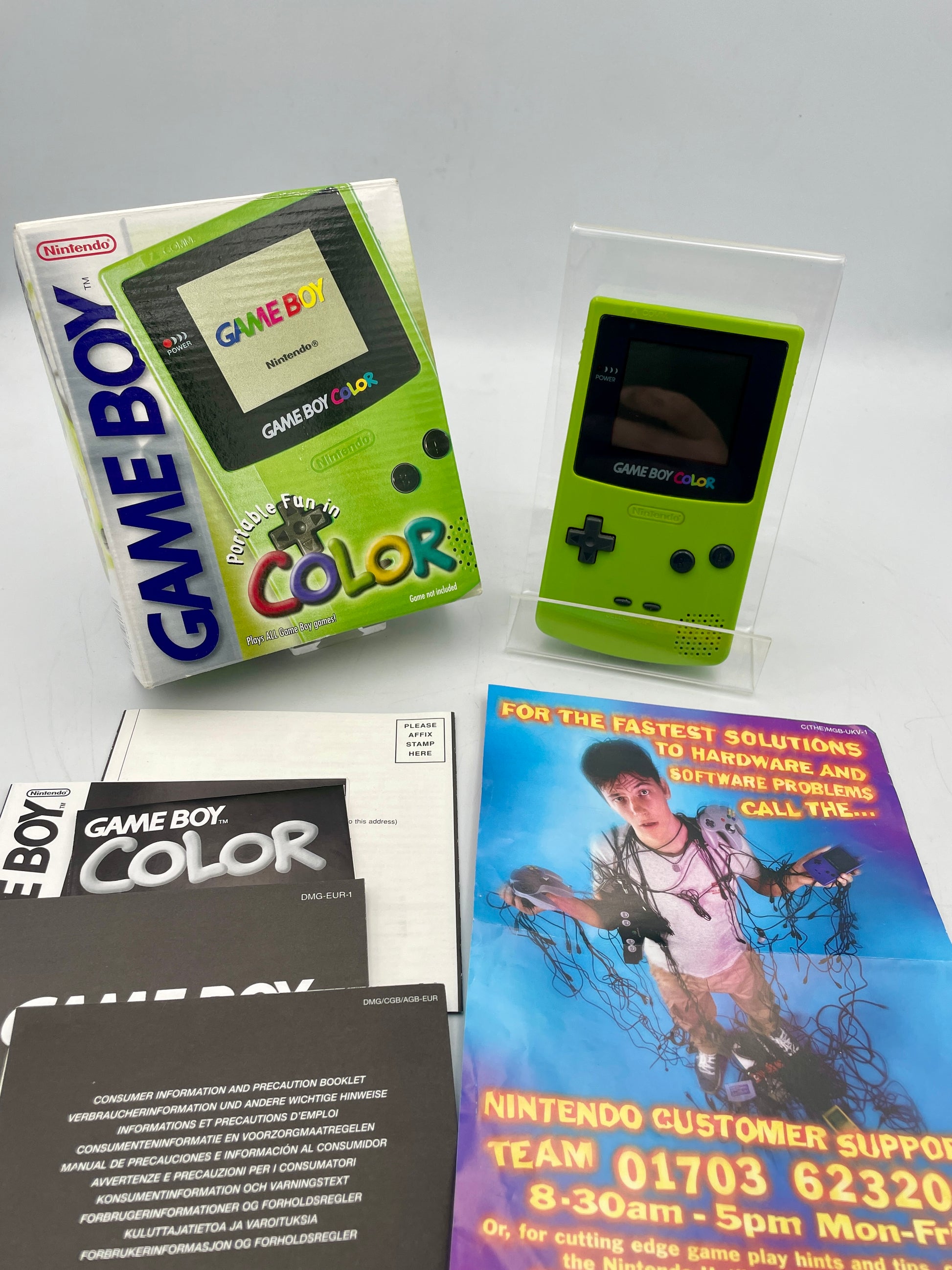Green Game Boy Color console with packaging and support information leaflets on a white background
