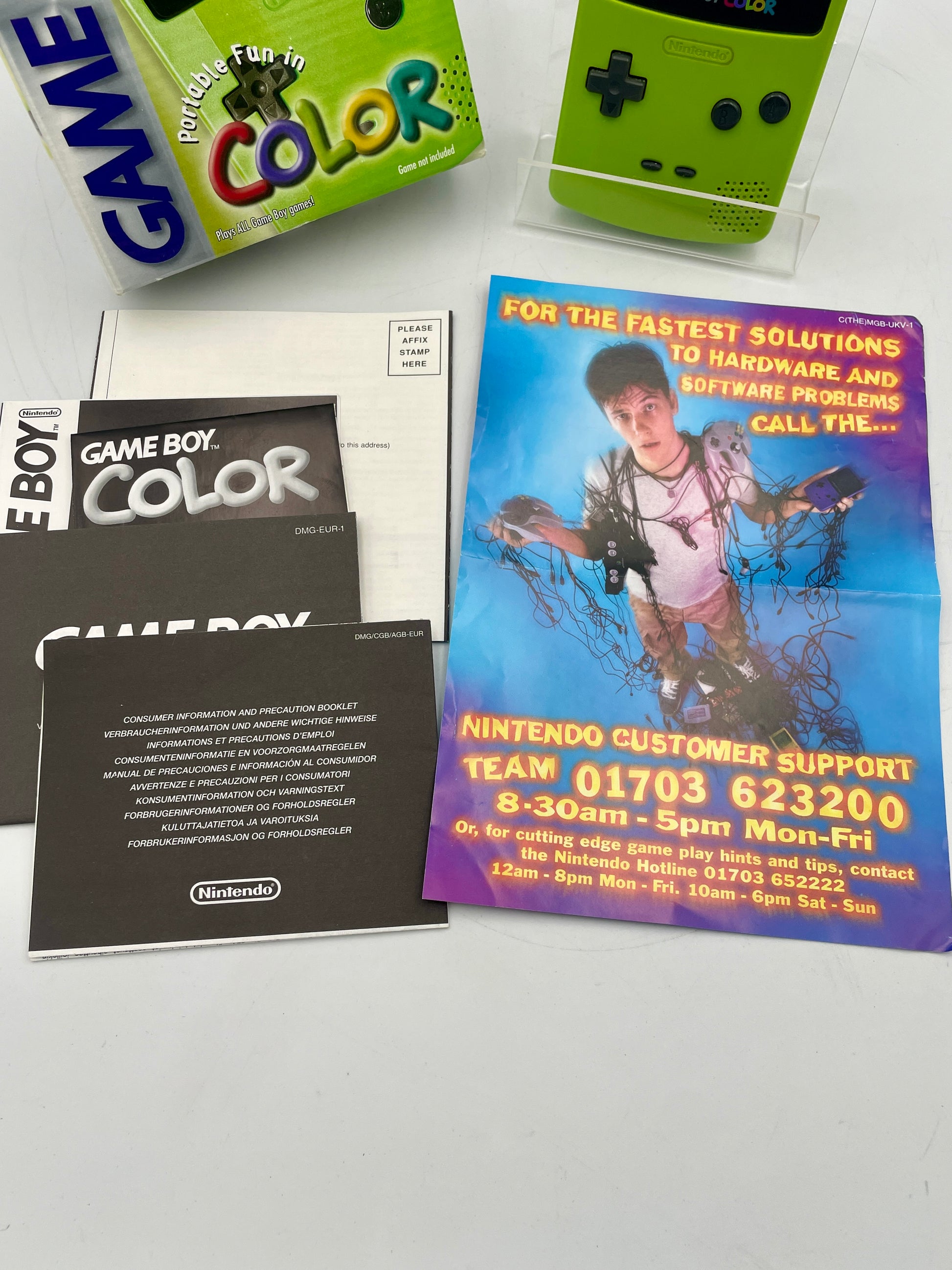 Collection of Game Boy Color items including a green console, packaging, and support leaflet.