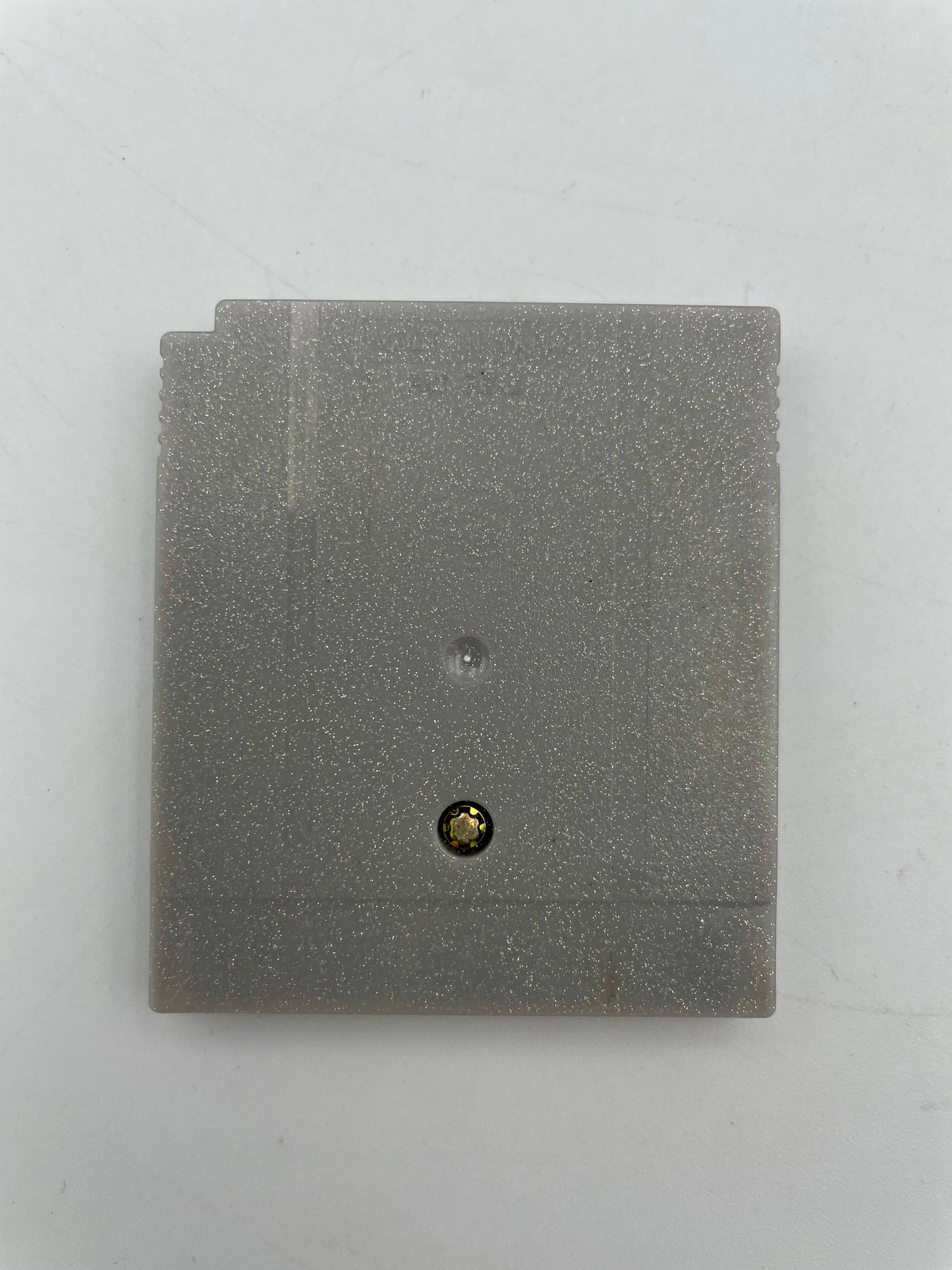 Gray square object with a small black and gold button on a white background