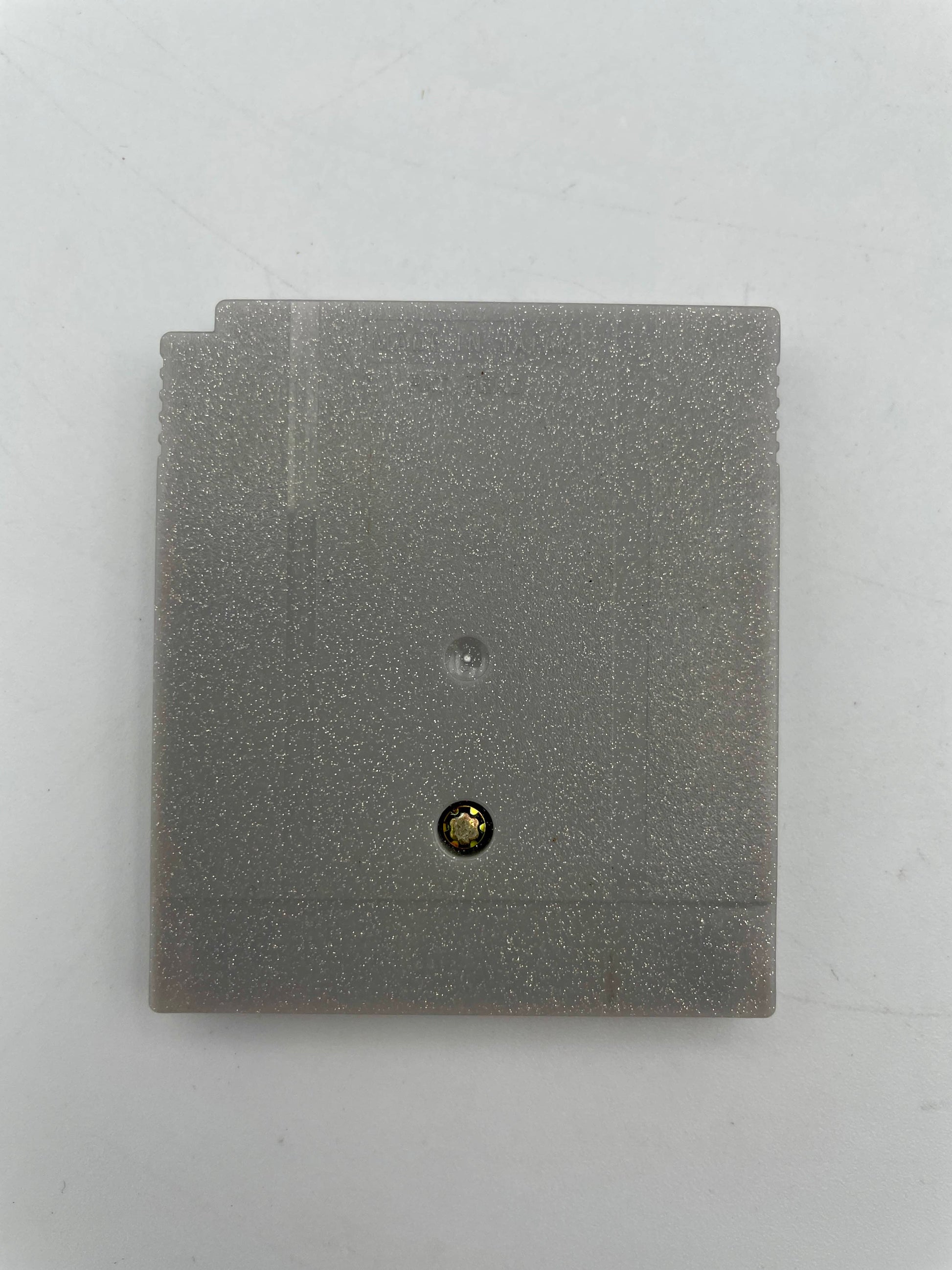 Gray square object with a small black and gold button on a white background