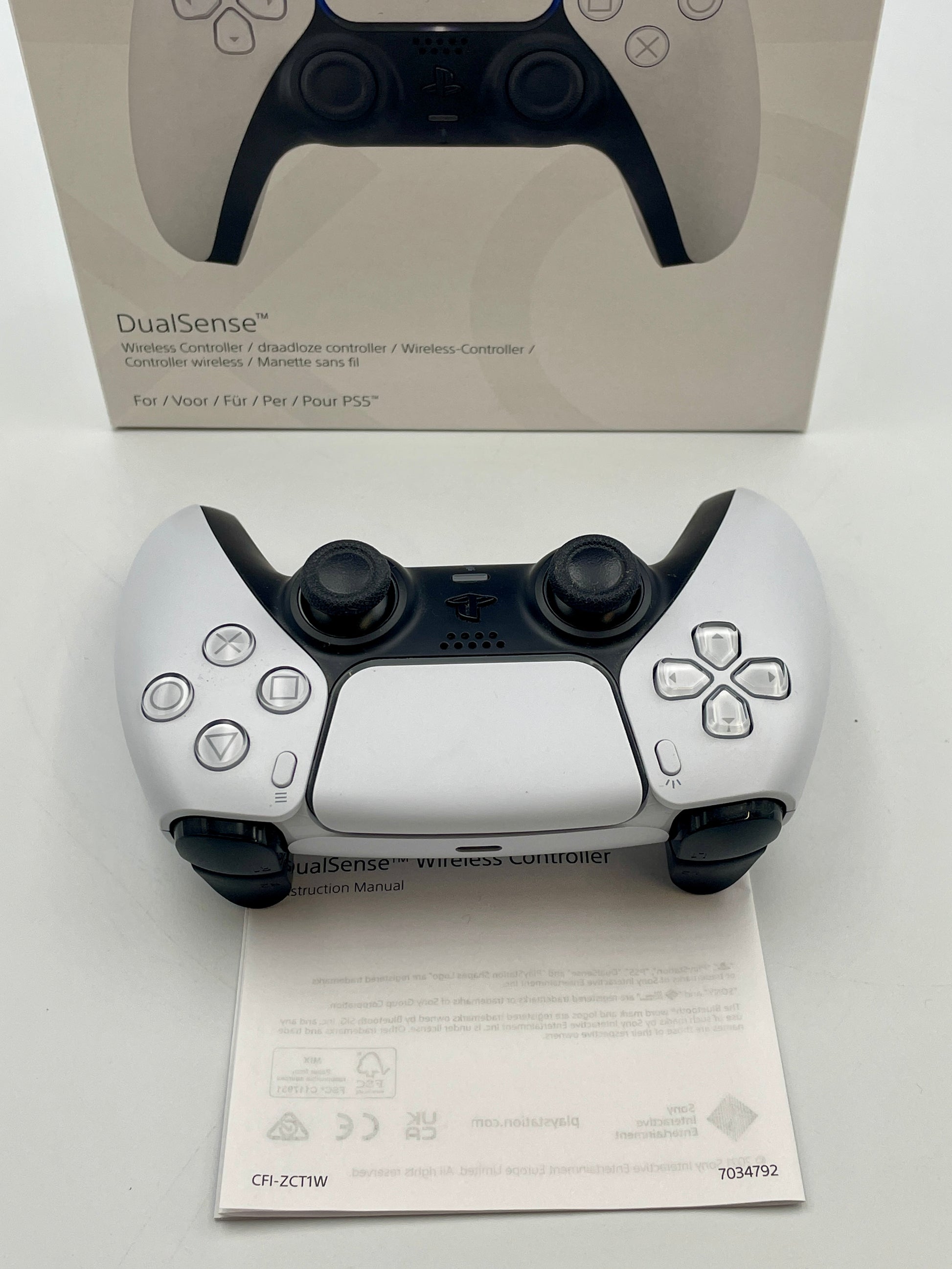 White gaming controller with black accents on a white surface, with a box and manual in the background.